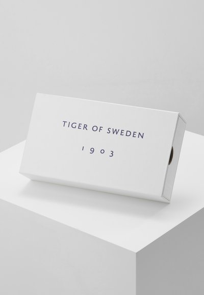 Balts taisnstūra kaste ar vāku, uz kuras priekšpuses tumši zilā krāsā ir izdrukāts "TIGER OF SWEDEN" un "1903". Gluda, matēta tekstūra.