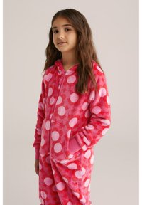 Rožinė flisinė vienaragė su dideliais baltais ir šviesiai rožiniais taškeliais. Yra priekinis užtrauktukas ir kišenės, su banguotais rožiniais rankogaliais.