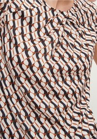 Robe sans manches en tissu à motifs avec des formes entrelacées en noir, blanc et terre cuite, texture lisse et détail de plis subtils.