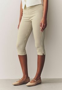Pantacourts ajustés longueur genoux, en motif à carreaux marron et crème, avec des fentes latérales à l'ourlet. Assorti à des chaussures plates de couleur claire.