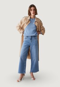 Beež värvi trentšmantel, helesinine soonikuline kampsun, kõrge vöökohaga helesinised laiade jalgadega teksad ja valged avatud varbaga kontsakingad.