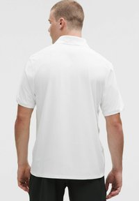 Biely polokošeľov�ý tričko s krátkym rukávom vyrobené z textúrovanej látky, s klasickým golierom a rovnými lemami, zobrazené zozadu.