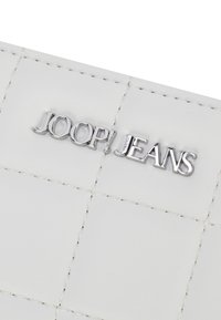 Portafoglio bianco con texture e un motivo trapuntato, caratterizzato da un logo metallico argento "JOOP! JEANS" ben in vista sul davanti.