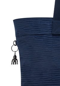 Mörkblå tygväska med en strukturerad mönstring, försedd med en nyckelringsaccessoar som föreställer en liten figur. Stadiga handtag och sydda sömmar.