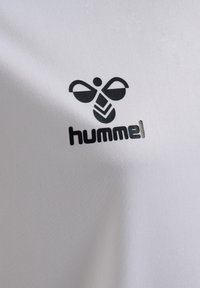 Witte performance shirt met een zwart Hummel-logo, bestaande uit gestileerde vleugels en een geometrisch patroon, op een soepele, gestructureerde stof.