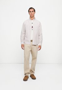 Button-up striped shirt in white and red, beige chino pants, and brown lace-up shoes. Simple design with a collared neck.