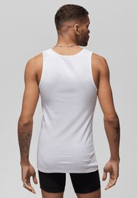 White sleeveless tank top made of ribbed cotton. Features a round neckline and a fitted design, worn with black shorts. Subtle texture visible.