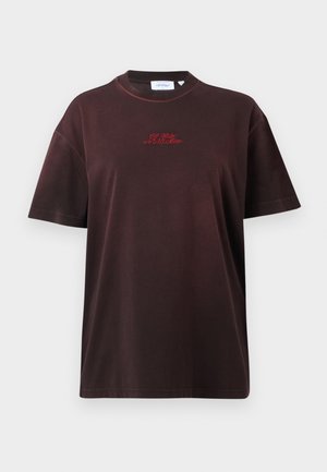 Žena s čiernymi slnečnými okuliarmi, tmavohnedým tričkom s červeným detailom, modrými džínsami, čiernymi sandálmi na podpätku a drží čiernu kabelku na ramene.