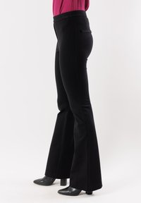 Pantaloni neri a zampa d'elefante realizzati in tessuto morbido, con vita aderente e dettaglio della tasca posteriore, abbinati a scarpe nere con tacco.