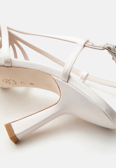 Λευκό σατέν πέδιλο με ψηλό τακούνι, λεπτά λουράκια στον αστράγαλο, κούμπωμα με αγκράφα και καφέ λάστιχο στη φτέρνα.