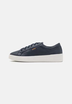 Sneaker bassa in pelle nera con lacci neri, suola spessa bianca e piccolo logo dorato "BOSS" sul lato.