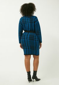 Vestido de patrón azul y negro con mangas largas, forma ajustada y cintura ceñida. Estilizado con botas negras hasta el tobillo.