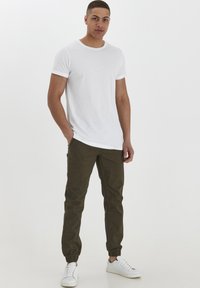 Vit crew-neck t-shirt, slim fit, kombinerad med olivgröna tapered byxor med elastiska mudd, och vita sneakers. Minimalistisk design.