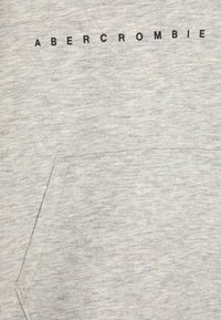 Grå sweatshirt med en mjuk textur, som har en framficka och "ABERCROMBIE" tryckt i svart över bröstet.