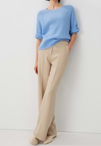 Pull à côtes bleu clair avec des manches retroussées associé à un pantalon droit beige. L'ensemble présente des lignes épurées et une coupe décontractée.