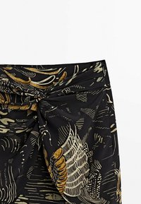 Black fabric with gold and light green abstract patterns, featuring pleats and a draped design at the waist. Smooth texture.
