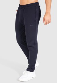 Pantalones jogger azul marino fabricados con material suave, que cuentan con una cintura elástica, bolsillos laterales y un pequeño logo en el muslo izquierdo.