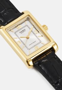Gold-tone quartz watch with a rectangular silver dial, black crocodile-embossed leather strap, and water-resistant marking.