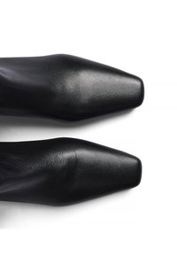 Zapatos de tacón alto de cuero negro con un diseño de punta afilada. Textura suave y silueta elegante, con un acabado brillante.