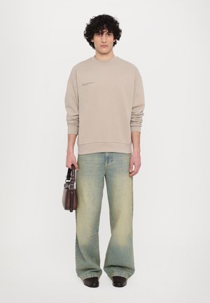 Beige sweatshirt with a round neckline and embroidered detailing, paired with light blue wide-leg jeans and a dark brown bag.