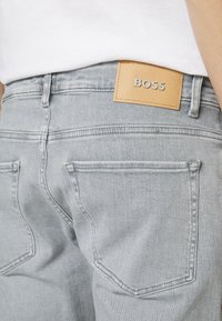 Jeans in denim grigio chiaro con una finitura testurizzata, dotati di due tasche posteriori e di una toppa in pelle color cuoio sul retro con la scritta "BOSS" impressa.