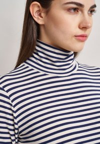 Gestreiftes Rollkragenoberteil mit navyblauen und weißen horizontalen Streifen, aus weichem, dehnbarem Stoff gefertigt. Enganliegendes Design mit hohem Kragen.