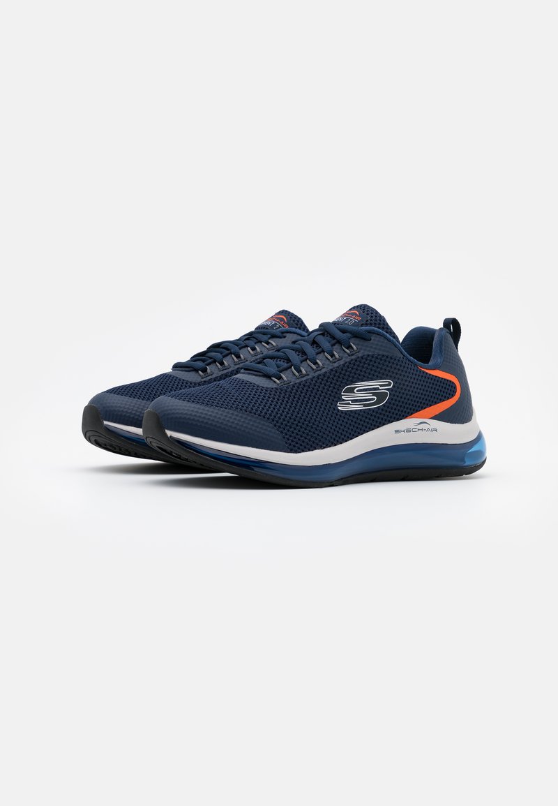 Zapatillas deportivas de malla en color azul marino con superficie texturizada, suela blanca y detalles en naranja. Cuentan con un diseño de cordones y un collar acolchado para mayor comodidad.