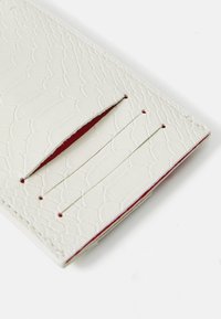 Cardholder alb din piele cu o suprafață texturată, solzoasă și un interior roșu. Dispune de multiple sloturi pentru carduri și accente de cusătură precise.