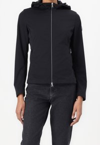 Svart lättviktsjacka med huva, framdragkedja och sidofickor. Har en slät yta och en figurnära design. Minimalistisk stil.