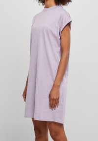 Lila Baumwollkleid mit hohem Kragen und kurzen Ärmeln. Locker geschnittene Silhouette, knielang, glatte Textur, minimalistisches Design.