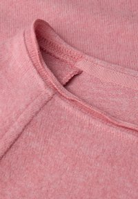 Różowy sweter z tkaniny o teksturowanym wykończeniu. Okrągły dekolt z prążkowanym wykończeniem, z delikatnymi różnicami w odcieniu i miękkości.