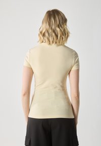 Short-sleeve, fitted top in light yellow fabric. Soft texture with a round neckline, smooth seams, and a plain design. Worn with black pants.