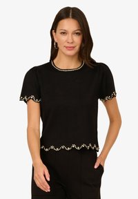 Černé tričko s krátkým rukávem a kulatým výstřihem, zdobené perlovými akcenty podél lemu a rukávů, s vlnitým designem.