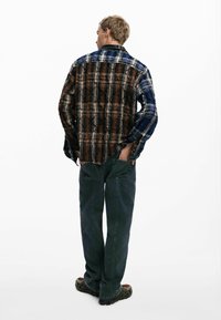 Plaid shirt with a mix of brown, blue, and black colors, featuring a collar, buttoned design, and long sleeves. Worn with green pants.