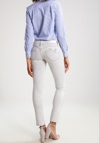 Jean skinny gris clair avec une texture lisse et des poches arrière, associé à une chemise à manches longues bleu et blanche à rayures et des talons beiges.