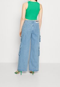 Pantalones cargo de mezclilla en azul claro, con pierna ancha y bolsillos laterales, combinados con una camiseta ajustada verde y sandalias de tacón verdes.