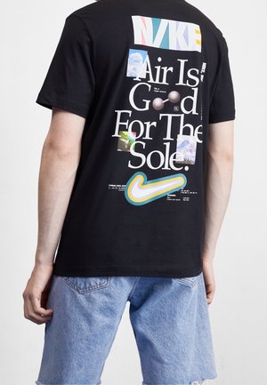 Personne portant un t-shirt Nike noir avec un logo Nike coloré et le texte « Air Is Good For The Sole » au-dessus d’un swoosh multicolore, associé à un short en jean clair.