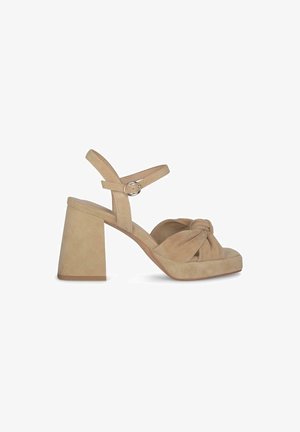Sandali platform in suede beige con dettaglio di nodo frontale e tacco a blocco largo. Cinturino alla caviglia regolabile con fibbia metallica circolare.