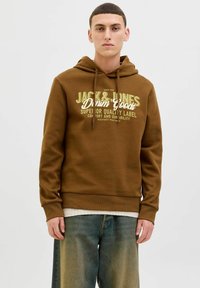 Brun hætte sweatshirt med grafisk tekst foran i creme og mørkegrøn. Blød tekstur, ribbede manchetter og taljebånd, båret over et hvidt lag.