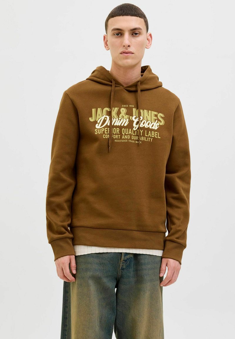Brun hætte sweatshirt med grafisk tekst foran i creme og mørkegrøn. Blød tekstur, ribbede manchetter og taljebånd, båret over et hvidt lag.