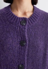 Cardigan viola lavorato a maglia con colletto a coste, dotato di quattro bottoni neri lungo la parte anteriore. Tessuto strutturato con dettagli di lavorazione irregolare.