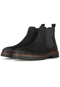 Botines de ante negro con paneles laterales elásticos, punta redonda y suela de goma. Cuentan con un pespunte marrón en contraste y lengüetas de agarre.