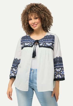 Weiße, locker sitzende Bluse mit blauen gestickten Akzenten an den Ärmeln und dem Ausschnitt, mit Quasten an der Vorderseite und floralen Mustern.