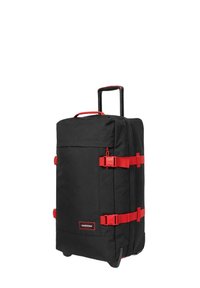 Maleta negra con ruedas, correas y acentos rojos, de forma rectangular, con tejido texturizado, mango telescópico y ruedas para rodar.