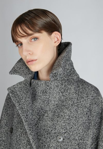 Cappotto grigio a spina di pesce con colletto alto, design doppiopetto e grandi bottoni neri. Tessuto di lana testurizzato con una vestibilità strutturata.