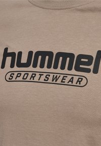 Lähikuva vaaleasta kankaasta, johon on painettu musta "hummel SPORTSWEAR" -logo.