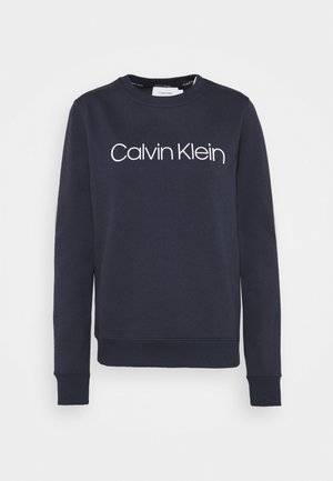Navyblauwe, lange mouwen crewneck-trui met een wit "Calvin Klein"-logo in het midden van de borst.