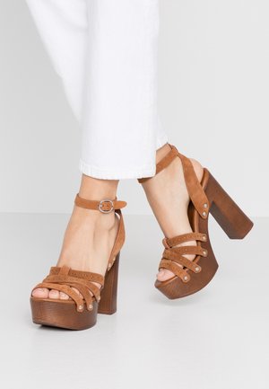 Sandales à talons hauts en daim marron avec une semelle compensée, dotées de plusieurs lanières croisées et d'une sangle à boucle à la cheville. Talon en bois.