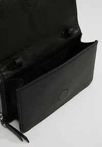 Czarna skórzana torba o fakturowanym wykończeniu, wyposażona w zapinaną na zamek komorę, płaską kieszeń oraz ozdobne paski. Wnętrze wydaje się przestronne i niepodszewkowane.