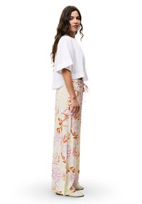 Weißes Cropped-Top mit weiten Ärmeln; gemusterte, lockere Hose in Pastellfarben mit floralen Designs; das Model trägt leichte Slipper.